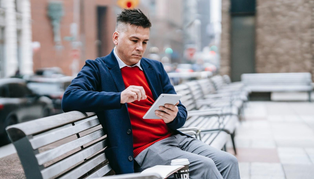 Man sitting on a bench, watching on his tablet.